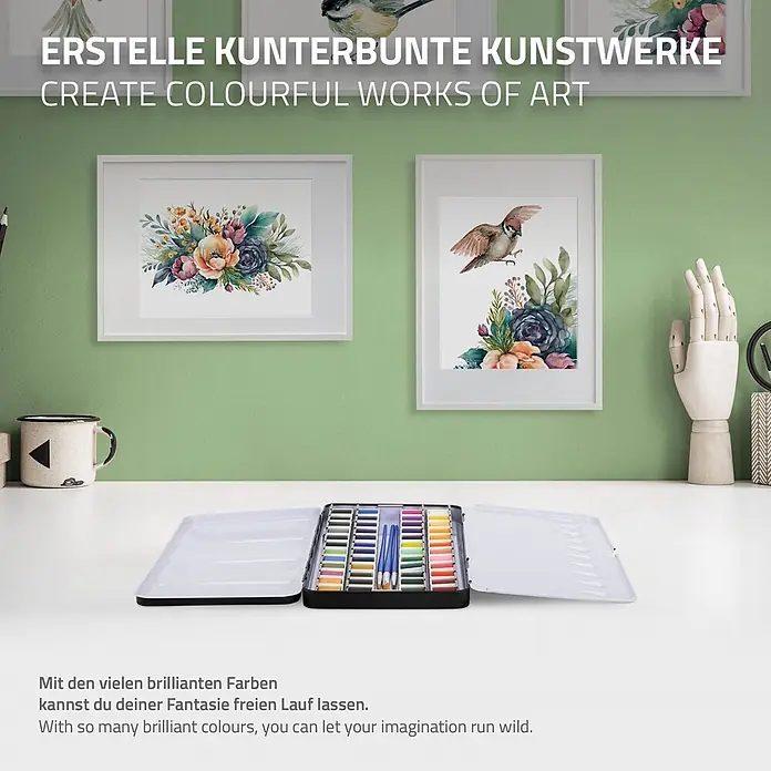 Aquarellfarben Set 48 Farben in tragbarer Box inkl. Utensilien -  - Ein Metallkoffer mit vielen leuchtenden Aquarellfarben und Pinseln, offen auf einem weißen Schreibtisch mit Kunstwerken im Hintergrund.