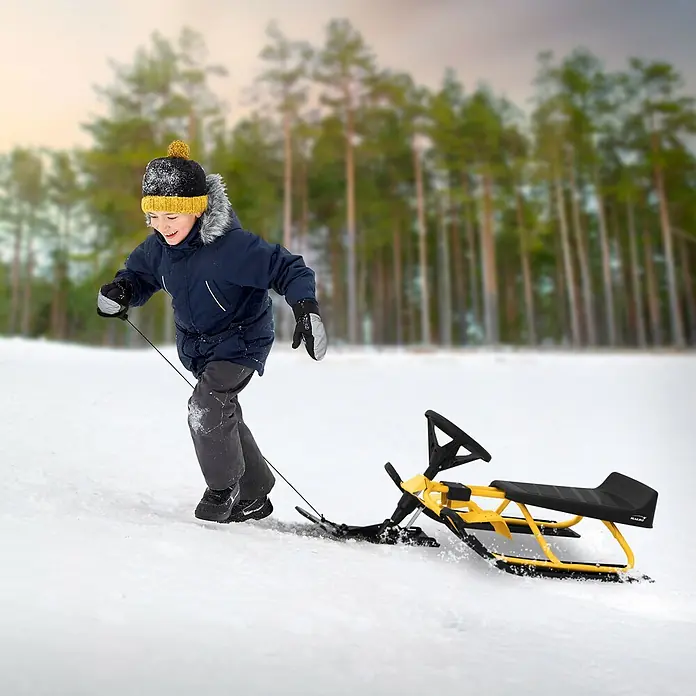 Lenkschlitten für Kinder Gelb 119 x 38 x 50 cm Stahlrahmen bis 90 kg -  - Ein Kind zieht einen gelb-schwarzen Lenkschlitten mit Lenkrad und Sitz durch den Schnee im Freien.