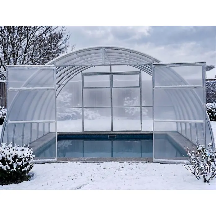 Garten Dream Poolüberdachung Sigma, 6mm Polycarbonat - L x B x H: 1.000 x 400 x 220 cm - Transparente Poolüberdachung mit Metallrahmen, teilweise geöffnet, schneebedeckt, schützt einen blauen Pool im Winter.