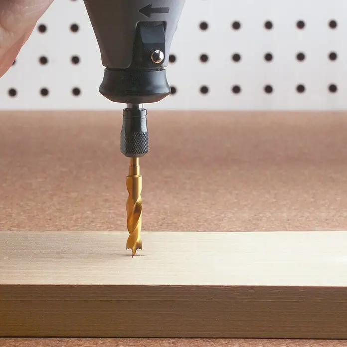 Dremel Holz-Bohrersatz Mod. 636 - 3 mm - 6 mm, 4 Stk. - Nahaufnahme eines goldenen Spiralbohrers, der in ein Holzbrett bohrt, ideal für präzise Holzarbeiten.
