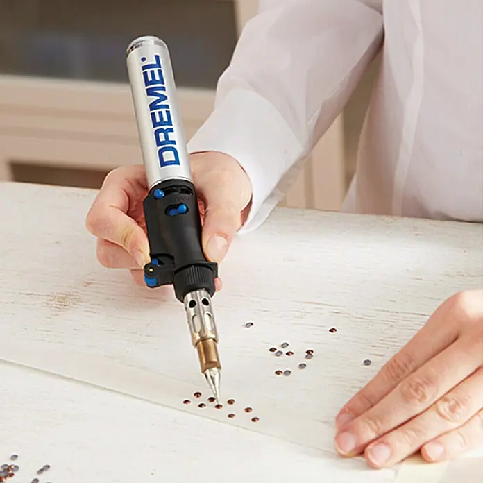 Dremel Lötspitze VersaTip Mod. 201 - 2 Stk. - Nahaufnahme einer Person, die einen Dremel VersaFlame-Brenner verwendet, um kleine Kristalle auf einem weißen Untergrund zu befestigen.