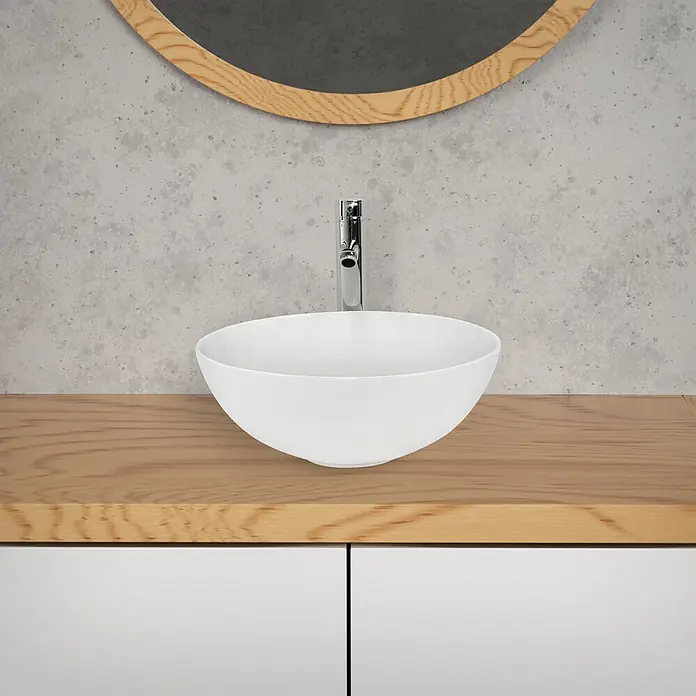 LuxeBath Waschbecken Keramik Waschtisch Ø 320x135 mm Rund Weiß Spülbecken -  - Weißes Aufsatzwaschbecken mit Chromarmatur auf heller Holzplatte, vor grauer Betonwand mit rundem Spiegel.