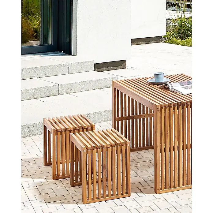 Beliani Gartenstuhl-Set BELLANO - 2 Stk., Akazienholz, Braun, B x T x H: 45 x 35 x 43 cm - Gestreifter Holztisch und zwei passende Hocker für die Terrasse. Auf dem Tisch stehen Tasse und Magazin.