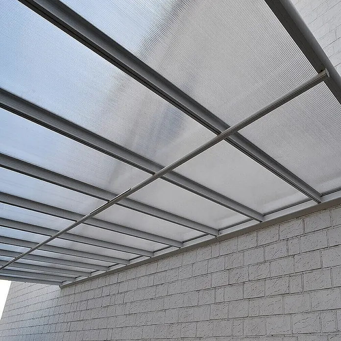 HOME DELUXE - Terrassenüberdachung SOLIS | Farbe: Weiß, Größe: 435 / 442 x 300 / 303 x 278 / 226 cm -  - Transparente, gerippte Polycarbonat-Überdachung mit grauem Metallrahmen über einer hellen Ziegelwand.