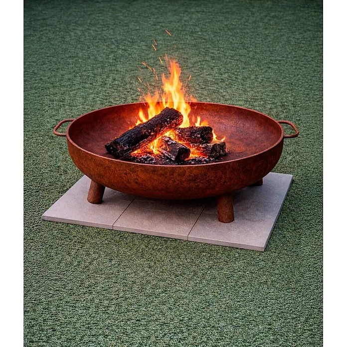 Nora Flames Brasero Calsotera con patas - Diámetro: 100 cm, Acero Corten - Fogón de acero color óxido con leños ardiendo, sobre losas de pavimento al aire libre.