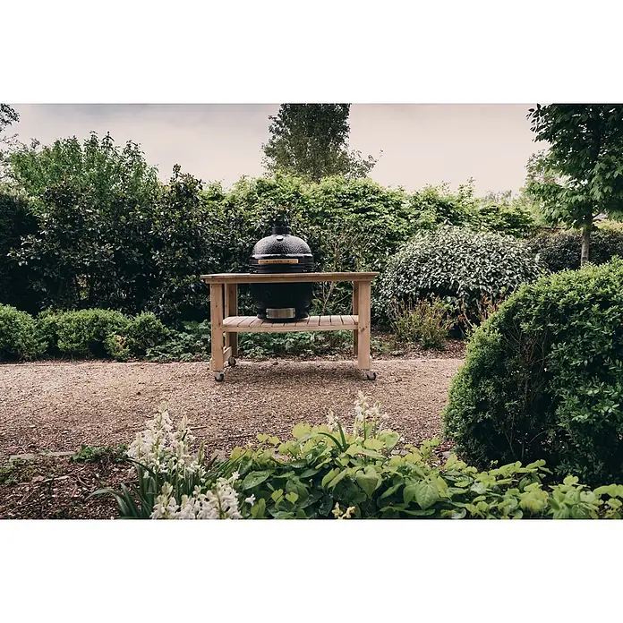 Outr Ahumador Kamado Grill Large - Diámetro de la superficie de la parrilla: 46,8 cm, Negro - Parrilla kamado negra sobre una mesa de madera con ruedas, ubicada en un jardín exuberante.