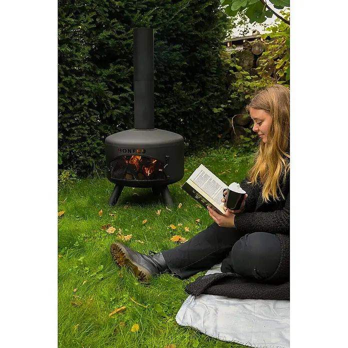 Bonfeu Chimenea de exterior Bongiro - Ø x Al: 55 x 132 cm, Acero, Negro - Chimenea de jardín Bonfeu de metal negro con fuego, calentando a una persona leyendo en el jardín.