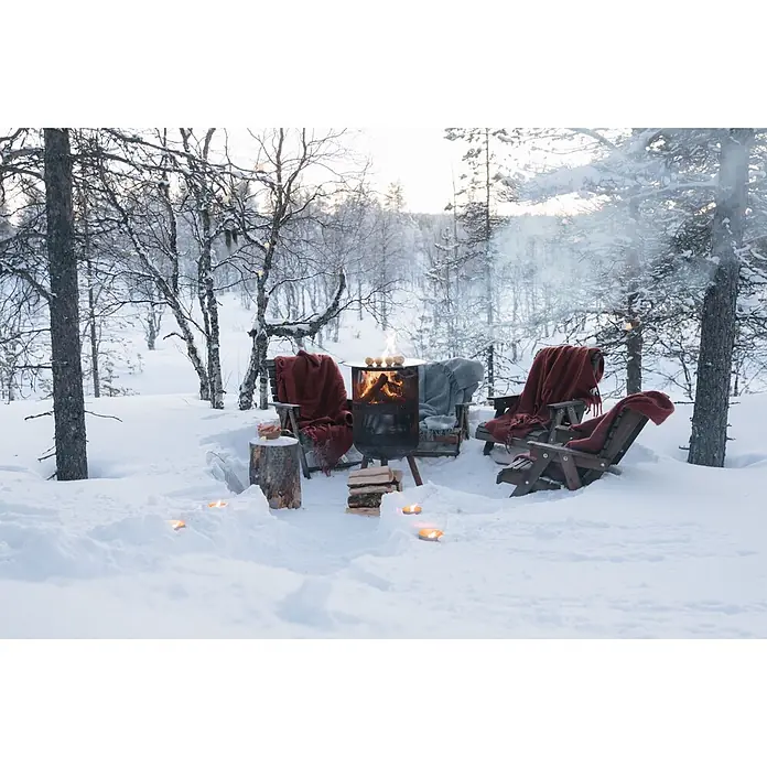 Bonfeu Chimenea de exterior Bonves - Ø x Al: 45 x 100 cm, Acero, Negro - Acogedora zona de asientos al aire libre en un bosque nevado con una hoguera encendida, dos sillas con mantas y pequeños fuegos en el suelo.