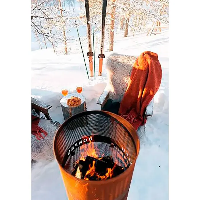 Bonfeu Chimenea de exterior Bonves - Ø x Al: 45 x 100 cm, Acero Corten, Marrón óxido - Brasero redondo de metal naranja Bonfire con rejilla y leña quemándose, en una zona de estar exterior nevada.