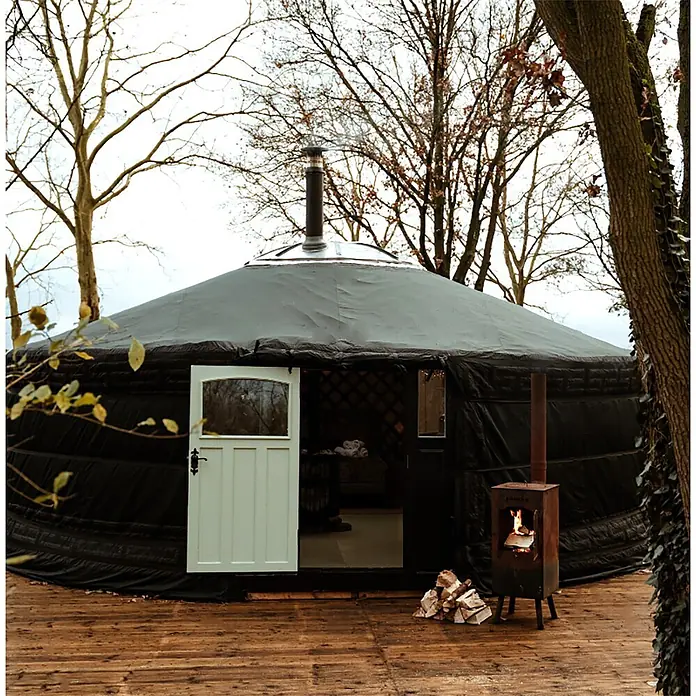 Bonfeu Chimenea de exterior Boncarre - L x An x Al: 35 x 35 x 164 cm, Acero Corten, Marrón óxido - Una yurta negra con puerta clara sobre una cubierta de madera, una estufa de leña encendida cerca.