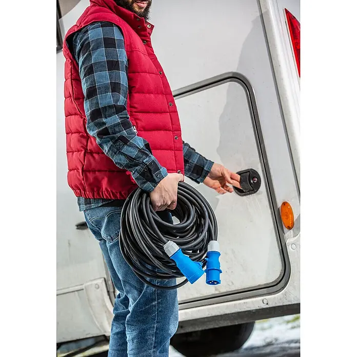as-schwabe Verlängerungskabel H07RN-F 3G2,5 - 10 m, Schwarz, IP44, H07RN-F - Mann hält aufgerolltes schwarzes Stromkabel mit blauen CEE-Steckern für Wohnmobil.