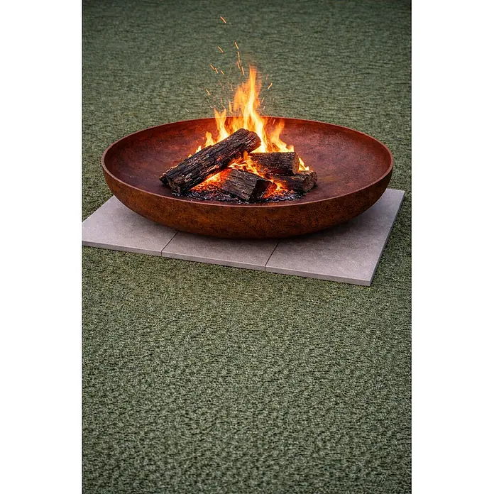 Nora Flames Brasero Calsotera - Diámetro: 80 cm, Acero Corten - Brasero marrón oxidado con troncos ardiendo, sobre adoquines claros.