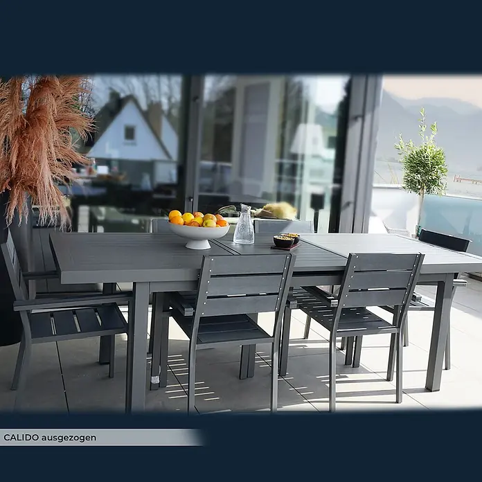 Home Deluxe Gartentisch CALIDO -  - Dunkelgraue ausziehbare Terrassen-Sitzgruppe mit Tisch und Stühlen, dekoriert mit Obst und Getränken.