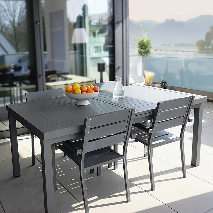 Home Deluxe Gartentisch CALIDO -  - Dunkelgrauer Lamellen-Gartentisch mit vier Stühlen auf einem modernen Balkon mit See- und Bergblick.