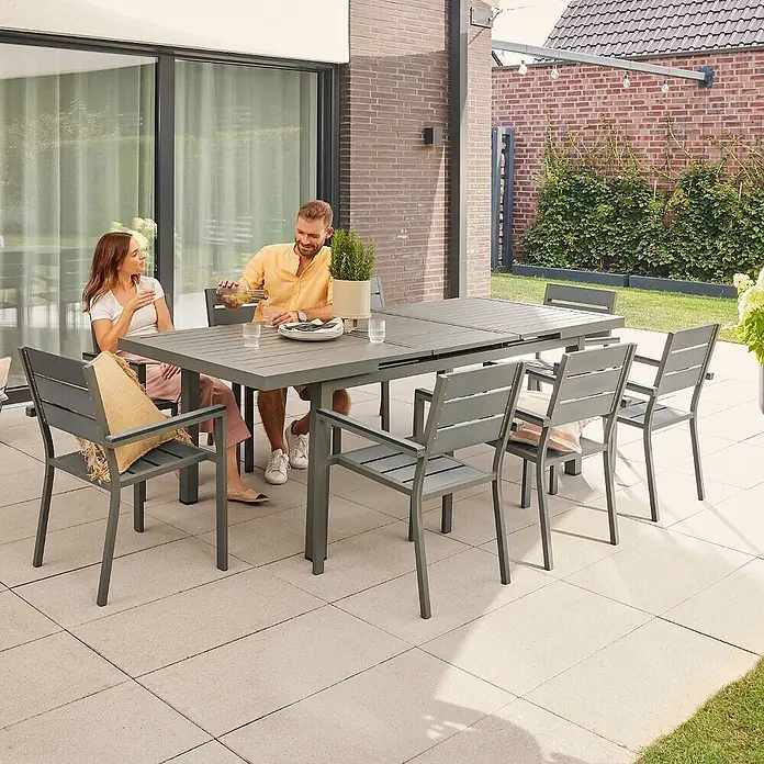 Home Deluxe Gartentisch CALIDO -  - Grauer Gartentisch mit passenden Stühlen auf einer Terrasse, von zwei Personen genutzt.