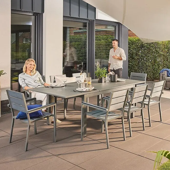 Home Deluxe Gartentisch CASA -  - Graue Outdoor-Essgruppe mit langem Tisch und Stühlen auf einer Terrasse, genutzt von Personen, die Getränke und eine Mahlzeit genießen.