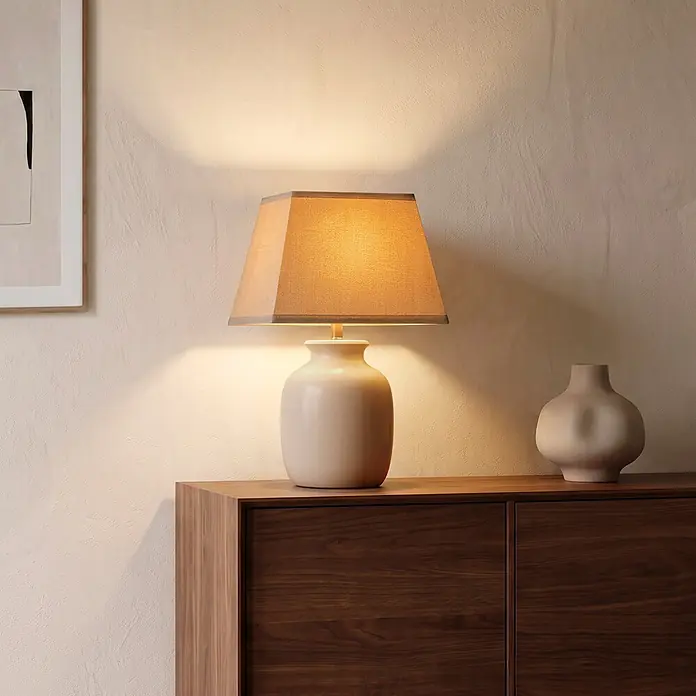 Home Sweet Home Lampenschirm Melrose - L x B x H: 20 x 20 x 14 cm, Taupe, Stoff, Eckig - Eine beigefarbene Keramiktischlampe mit Stoffschirm beleuchtet einen Raum, platziert auf einem Holzschrank neben einer dekorativen Vase.
