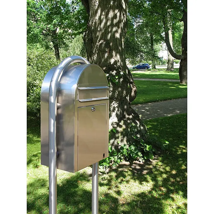 Proregal Wandbriefkasten Miami - Silber, Metall - Eleganter Edelstahl-Briefkasten mit gewölbter Oberseite und abschließbarer Tür, auf Pfosten in einem Park.