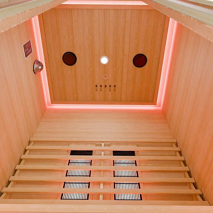 Infrarotkabine/Wärmekabine Nyborg S120V mit Vollspektrum-, Flächenstrahler & Hemlockholz -  - Innenansicht einer Holzsauna aus hellem Holz, mit Infrarot-Heizelementen am Boden und roter Ambientebeleuchtung.