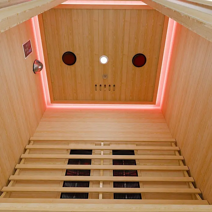 Infrarotkabine Nyborg S120K LED-Farblicht, 5 Keramik- 1 Flächenstrahler -  - Innenansicht einer hellen Infrarotsauna aus Holz mit rot glühenden Heizelementen und Umgebungsbeleuchtung.