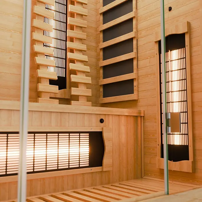 Infrarotkabine Kiruna130 Premium -  - Innenansicht einer hellen Infrarotsauna aus Holz mit leuchtenden Heizstrahlern hinter Holz- und Metallgittern.