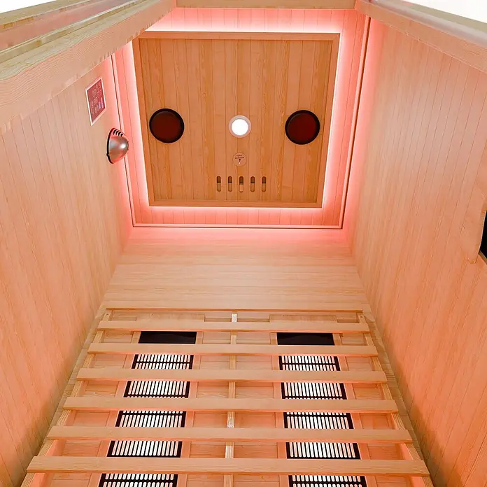 Infrarotkabine/Wärmekabine Nyborg S90V mit Vollspektrum-, Flächenstrahler & Hemlockholz -  - Innenansicht einer Infrarotsauna aus hellem Holz mit roter Beleuchtung und Heizstrahlern.