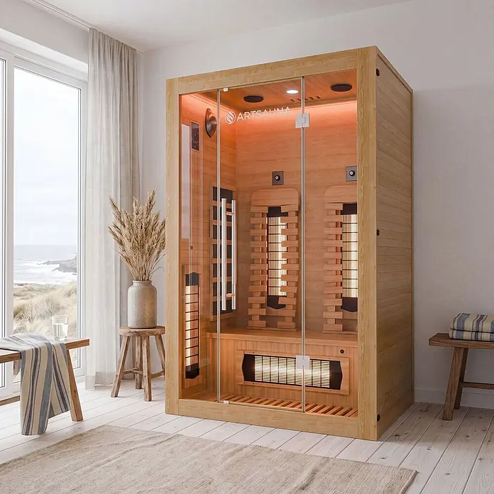 Infrarotkabine Kiruna130 Premium -  - Helle Holz-Infrarotsauna mit Glastür und warmer Innenbeleuchtung in einem hellen Raum mit Meerblick.