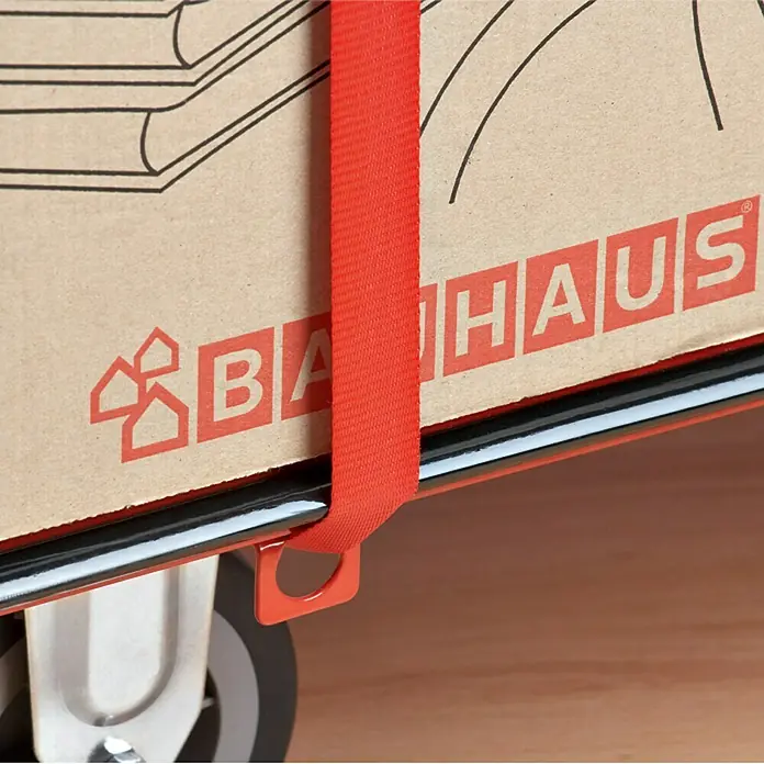 BAUHAUS Plattformwagen - Höhenverstellung: 87 cm - 105 cm, Stahl, 300 kg, Klappbar - Detailaufnahme eines Transportwagens mit einem Karton der Marke Bauhaus, gesichert mit einem roten Spanngurt. Praktisch für Umzüge und Transporte.