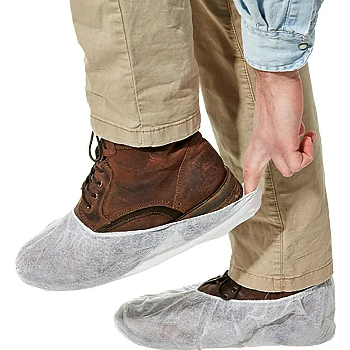 Wisent Protector para el calzado - 10 ud., Apto para: Zapatos hasta la talla 46 - La imagen muestra a un hombre poniéndose cubrezapatos blancos sobre sus botas de cuero marrón para mantener el suelo limpio.