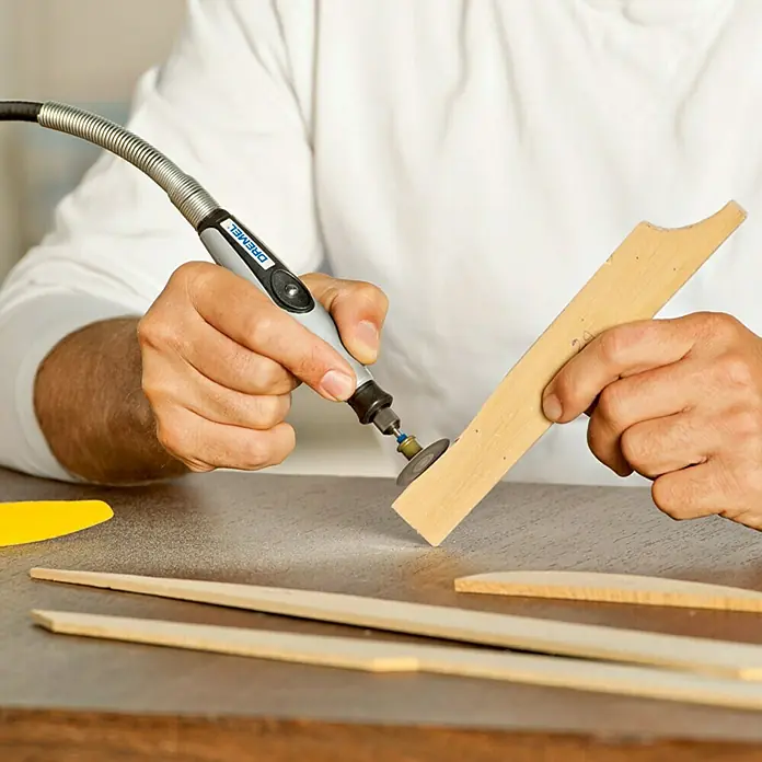 Dremel EZ SpeedClic Schleifscheibe Mod. SC 411 - 30 mm, Körnung: 60, 6 Stk. - Ein Mann benutzt ein Dremel-Werkzeug mit biegsamer Welle, um ein Stück Holz zu bearbeiten. Präzision und Vielseitigkeit für Hobby und Handwerk.