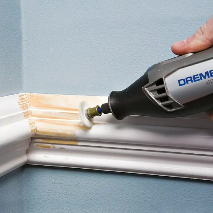 Dremel EZ SpeedClic Feinschleifbürste Mod. 471 S - 25 mm, Körnung: 36, Passend für: Dremel EZ SpeedClic Aufspanndorn Mod. SC 402 - Nahaufnahme eines Dremel 4000 Multifunktionswerkzeugs, das zum Schleifen einer weißen Fußleiste an einer hellblauen Wand verwendet wird.
