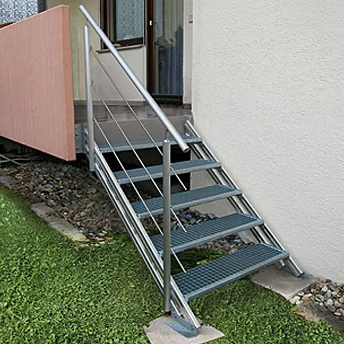 Treba Frewa Alaska Treppenstufe - Lochblech, 27 x 100 cm - Metalltreppe mit Geländer. Die Außentreppe mit Gitterstufen und Edelstahlhandlauf führt zu einer Haustür.