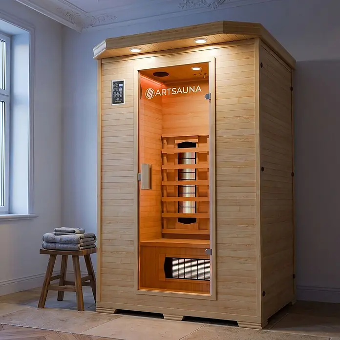 Infrarotkabine Oslo mit Vollspektrumstrahler -  - Eine freistehende hellholzige Saunakabine mit Glastür, glühenden Innenheizungen und Bedienfeld, drinnen mit Hocker und Handtüchern.