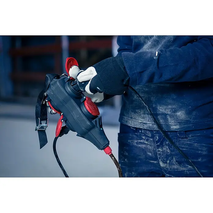 Brennenstuhl Kabeltrommel mit Powerblock KC 3200 5 - Kunststoff, 38 m, H07RN-F, IP44 - Person mit Arbeitshandschuhen hält schwarze und rote Stromverteilerbox mit mehreren abgedeckten Steckdosen und Gurt, angeschlossen an schwarzes Kabel.