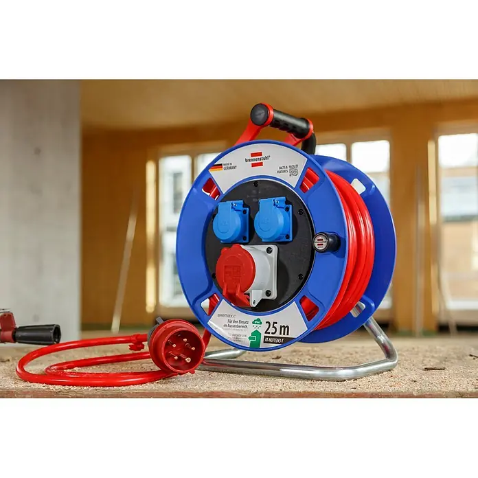 Brennenstuhl Kabeltrommel Garant CEE 1 AT-N07V3V3-G 5G1,5 - Kunststoff, 25 m, IP44 - Rot-blaue brennenstuhl Kabeltrommel mit drei Steckdosen und rotem Industriestecker, auf einer staubigen Baustelle gezeigt.