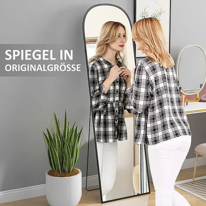 Homcom Standspiegel - Schwarz, Glas - Frau prüft ihr Outfit in einem schwarz gerahmten, bogenförmigen Ganzkörperspiegel in einem Raum.