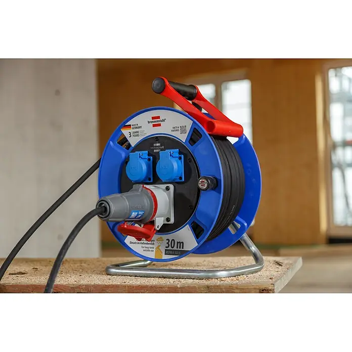 Brennenstuhl Kabeltrommel Garant CEE 1 - Kunststoff, 30 m, H07RN-F, IP44 - Blaue Brennenstuhl 30m Kabeltrommel mit rotem Griff und mehreren Steckdosen, für den langfristigen Außeneinsatz, auf Holz.