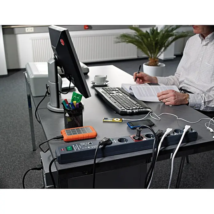 Brennenstuhl Secure-Tec Steckdosenleiste - 8-fach, Anthrazit, Kabellänge: 3 m, Mit Schalter - Dunkelgraue Steckdosenleiste auf einem Bürotisch, versorgt Computer, Smartphone und andere Geräte.