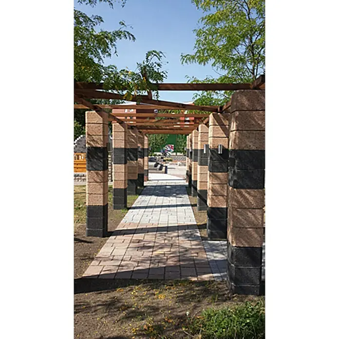 EHL Planomur Mauerstein Pfeilerstein - Anthrazit, 32,5 x 32,5 x 20 cm, Beton - Ein sonniger Weg führt durch eine Pergola mit gestreiften Steinsäulen, die einen einladenden Schatten spenden. Die Pflastersteine bilden ein harmonisches Muster.