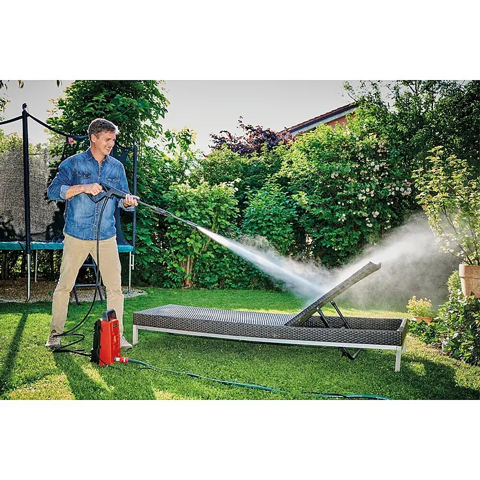 Einhell Classic Hochdruckreiniger TC-HP 90 - 1.200 W, Fördermenge: 372 l/h - Ein Mann reinigt eine dunkle Sonnenliege mit einem roten Hochdruckreiniger im Freien.