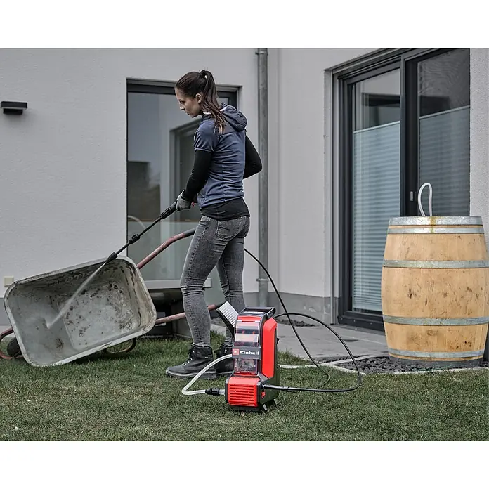 Einhell PXC 18V Akku-Hochdruckreiniger Hypresso 36/105 - 36 V, Ohne Akku - Roter und schwarzer Einhell Hochdruckreiniger, von einer Frau zum Reinigen einer Schubkarre im Freien verwendet.