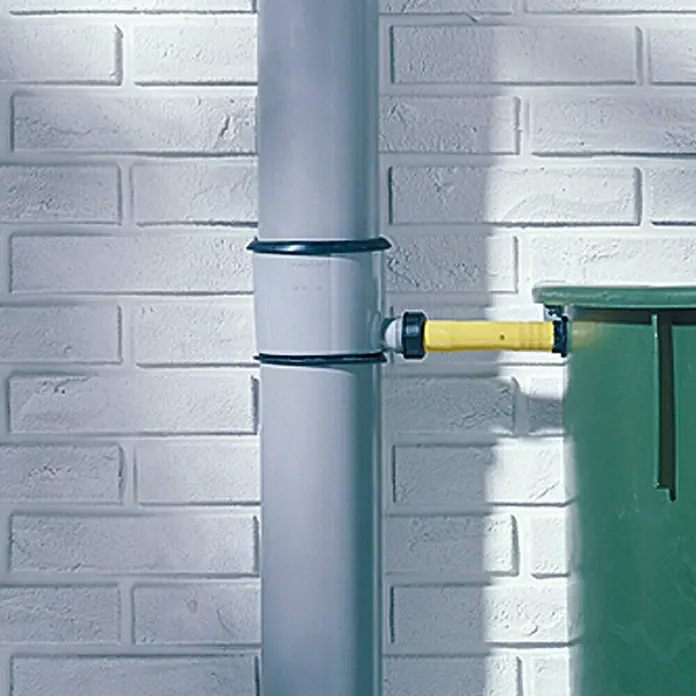 Marley Regensammler - Nennweite: 75 mm, Grau - Detailaufnahme eines Regenwasser-Fallrohrfilters mit Anschluss für eine Regentonne, installiert an einer weißen Ziegelwand.