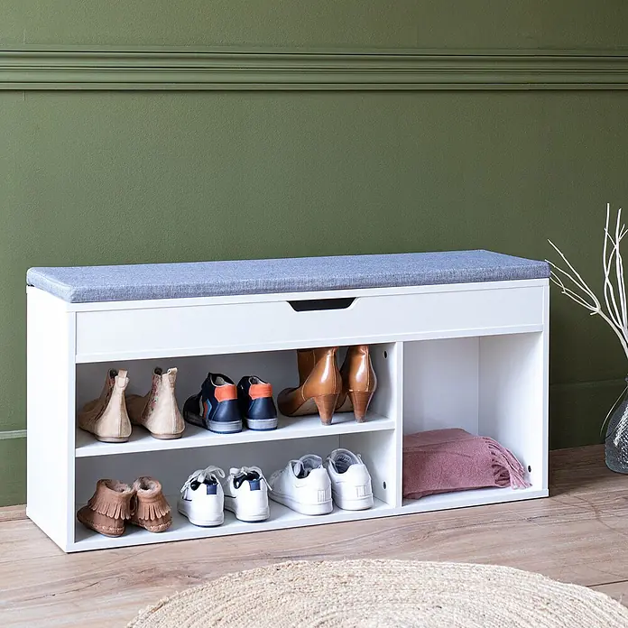 Happy Garden Schuhschrank ALAN - Weiß - Weißer Schuhschrank mit grauem Polster, bietet Stauraum für verschiedene Schuhe und eine gefaltete pinkfarbene Decke.