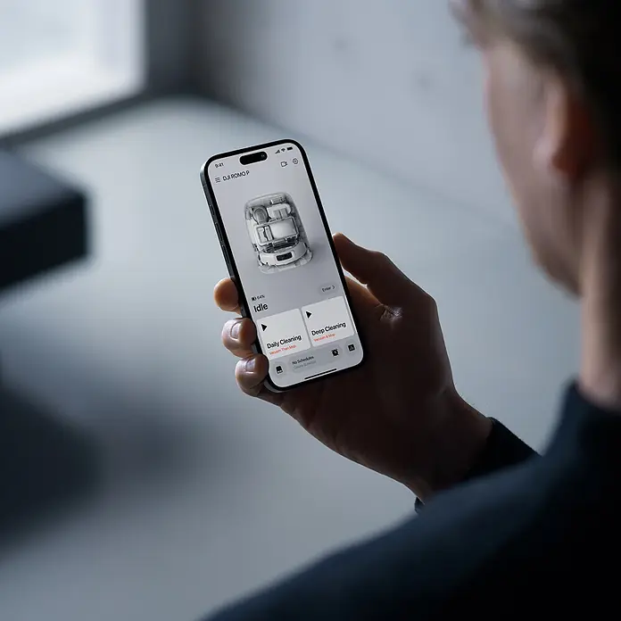 DJI Saugwischroboter P - Saugkraft: 25.000 Pa, Akkulaufzeit: 180 min, Fassungsvermögen Roboter: 260 ml - Eine Person hält ein schwarzes Smartphone mit einer App für einen Saugroboter, die Reinigungsoptionen und eine 3D-Ansicht zeigt.