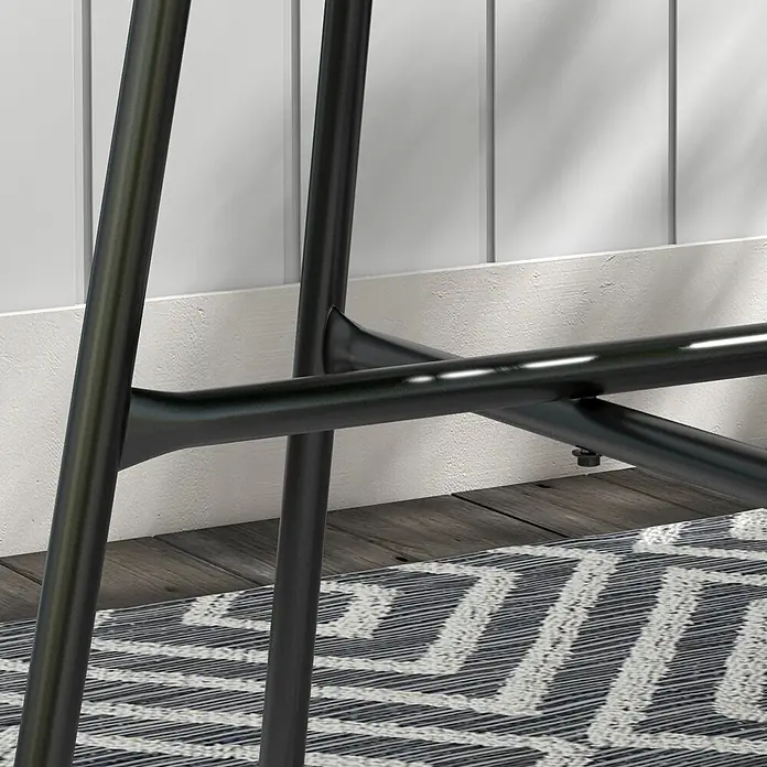 Furnicato Rattan-Beistelltisch schwarz, 50x50x50 cm -  - Nahaufnahme von schwarzen Metallhockerbeinen und Fußstütze auf einem gemusterten Teppich vor einer weißen Paneelwand.