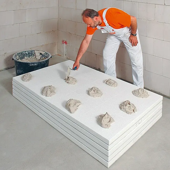 Fermacell Ansetzbinder - 20 kg - Mann trägt Kleber auf Dämmplatten auf. Die Platten sind aus Styropor und werden zum Isolieren von Gebäuden verwendet.