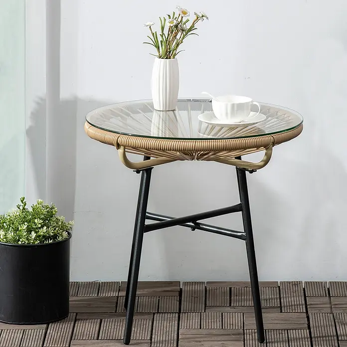 Outsunny Garten-Beistelltisch rund im Boho-Stil - Eisen, PE-Rattan, Beige - Runder Rattan-Beistelltisch für den Außenbereich mit Glasplatte und schwarzen Metallbeinen, darauf eine Blumenvase und eine Tasse.