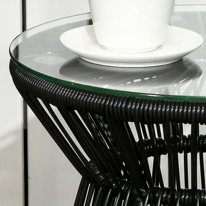 Outsunny Garten-Beistelltisch rund im Boho-Stil - Metall, PE-Rattan, Schwarz - Schwarzer geflochtener Beistelltisch mit Glasplatte, darauf eine weiße Tasse mit Untertasse.