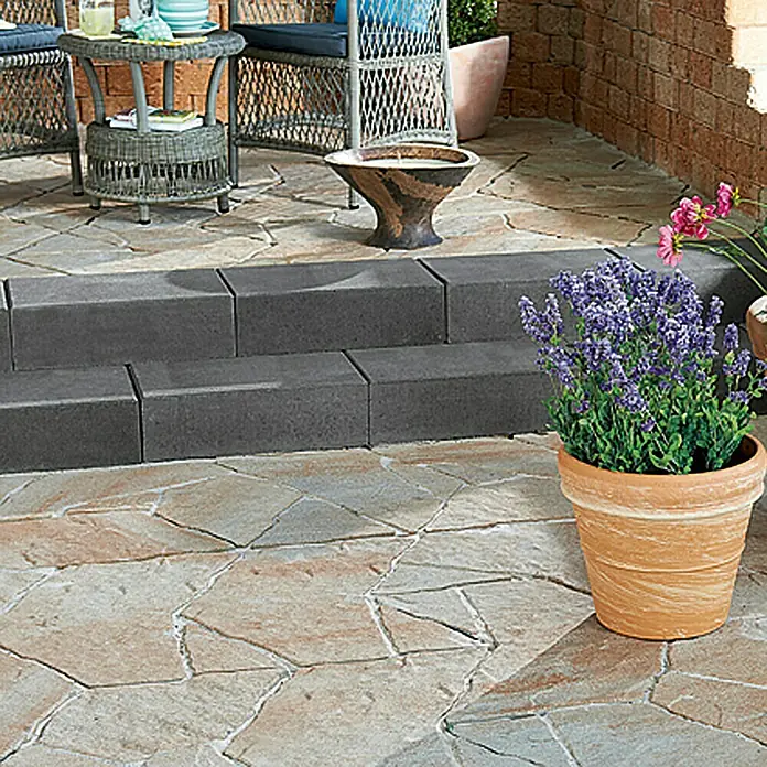 EHL Blockstufe - Anthrazit, 50 x 35 x 15 cm, Beton - Ein Außenbereich mit einem Pflasterweg, der zu einer Terrasse mit Gartenmöbeln führt, dekoriert mit einem Terrakotta-Blumentopf.