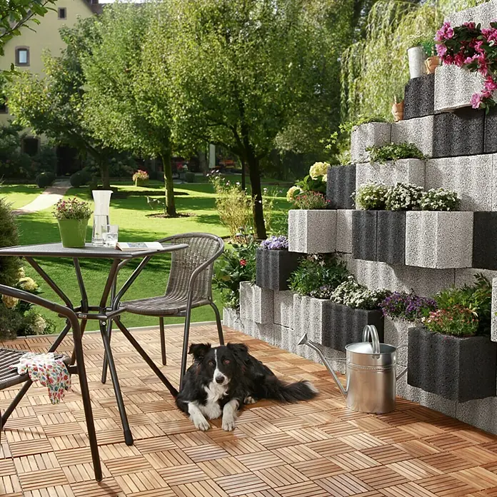 Christoph Pflanzstein Rasterstein - Anthrazit, 40 x 20 x 25 cm, Beton - Gartenmöbel mit Tisch, Stühlen und Hund auf einer Terrasse mit dekorativer Blockwandbepflanzung.
